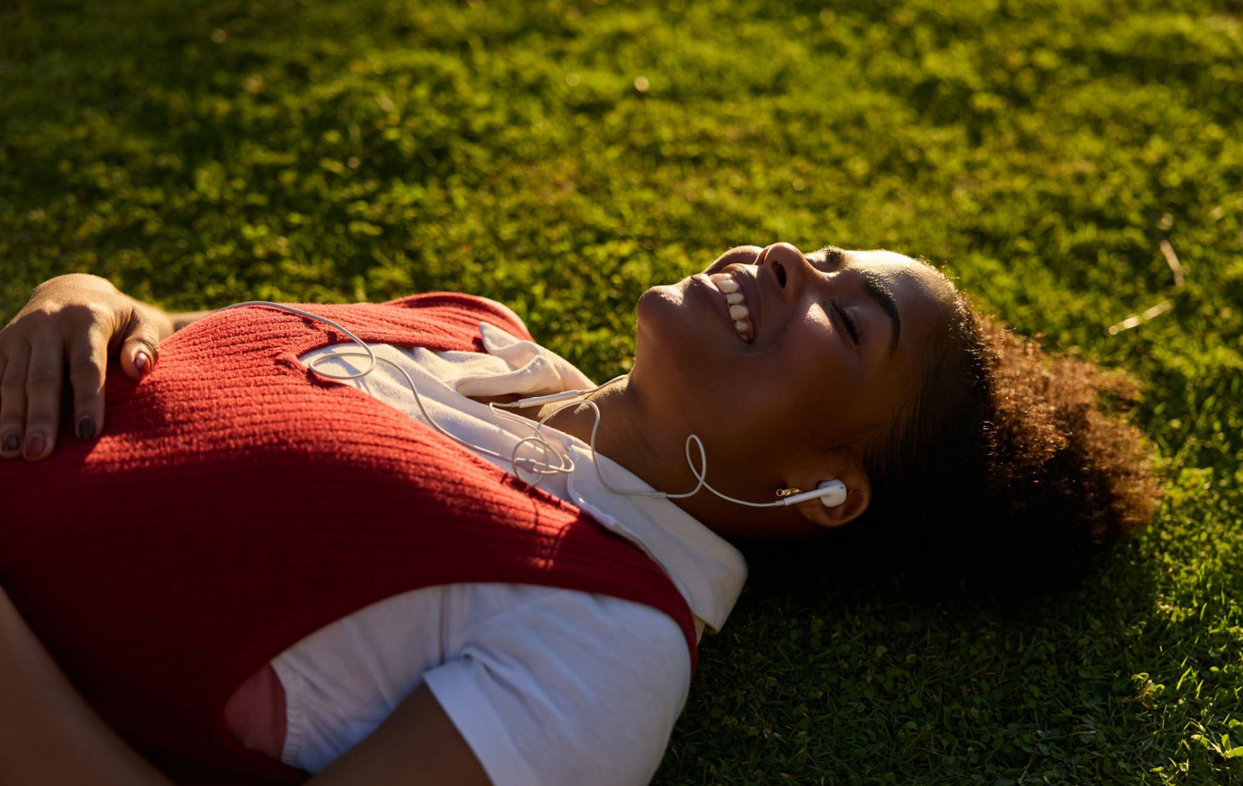 A woman lying on the grass in the sun, listening to music
