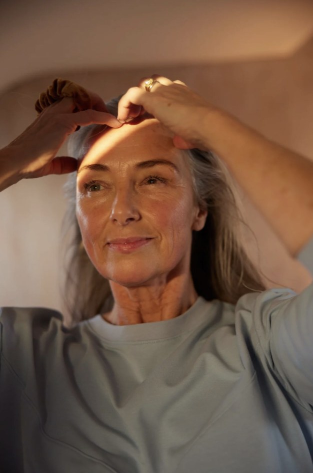 A woman tying her hair up, lit by warm daylight